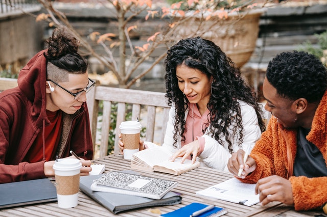 three students studying at a picnic table outside